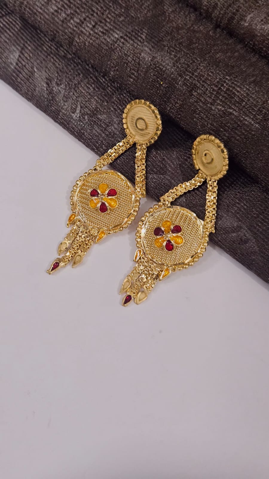 Gold earrings with red and yellow stones on a gray background